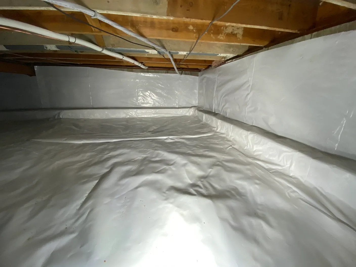 Crawl space encapsulado bajo una vivienda, con el suelo y las paredes de cimentación cubiertos por una barrera de vapor de plástico blanco reforzado sellada en las juntas.